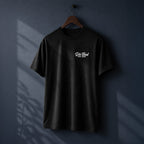 A black short-sleeve t-shirt hanging on a wooden hanger against a dark blue wall, featuring a small white 'DIE TIRED EST. 2017" hand written cursive logo printed on the chest.