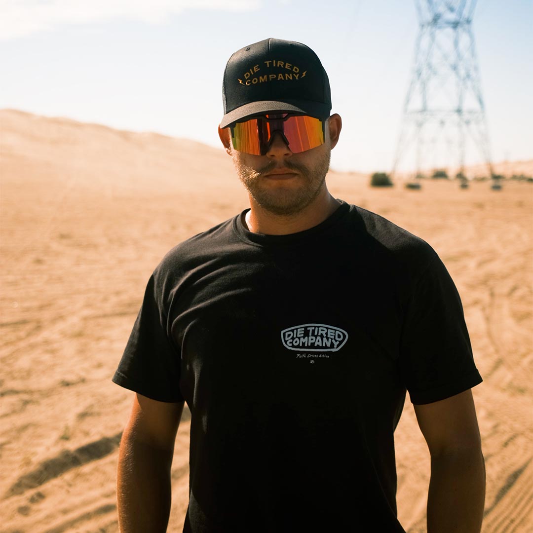 Man wearing Die Tired black cotton wildland firefighter T Shirt in the desert from the front.
