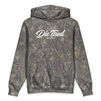 A long-sleeve pullover hoodie with a gray and brown tree bark camouflage pattern, featuring a white script graphic on the chest that reads 'Die Tired EST. 2017'.