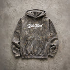 A pullover hoodie with a brown and gray tree-branch camouflage pattern, featuring a white 'Die Thied ESTD 2019' logo printed on the chest, laid flat on a textured gray concrete surface.