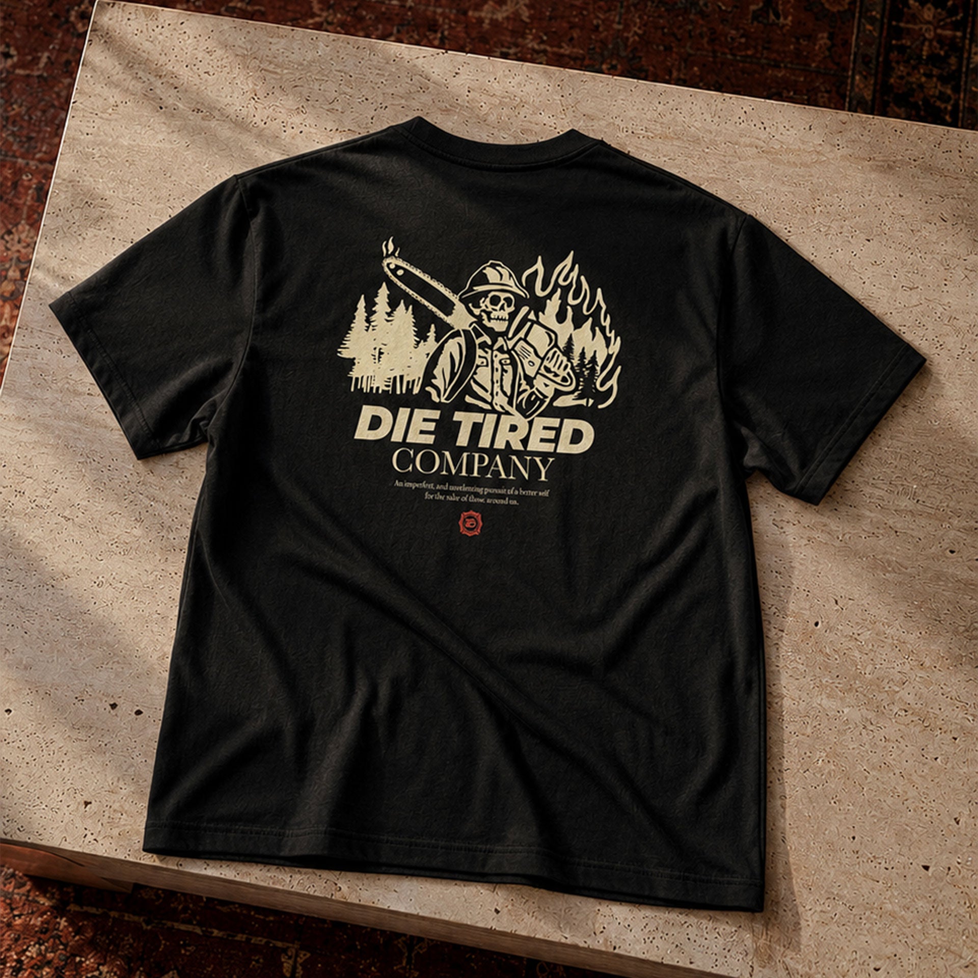Black t-shirt with 'Die Tired Company' wildland firefighter graphic on a stone surface