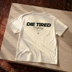 White t-shirt with 'Die Tired Company' text on a textured surface