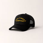 black trucker cap with a yellow "Die Tired Company" logo on a light gray background
