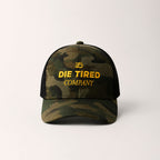 Camouflage trucker cap with 'Die Tired Company' yellow embroidered logo on a white background