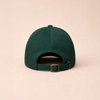 Green baseball cap on a beige background showing adjustable metal clasp