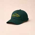 Green cap with yellow embroidered logo that says "Die Tired Company" on a beige background