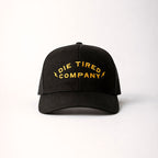 mens black trucker hat with yellow embroidered logo on front that says "Die Tired Company" on white background.